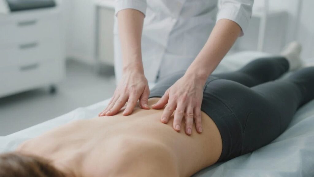 Osteopatia ginekologiczna: gdy lekarz mówi, że "taka Twoja uroda". 2 Profesjonalne dłonie osteopatki wykonujące delikatną terapię manualną na plecach pacjentki w gabinecie.
